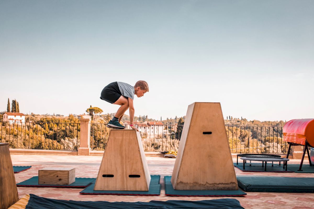 Kind bewegt sich über Parkour‑Elemente auf einer Terrasse.