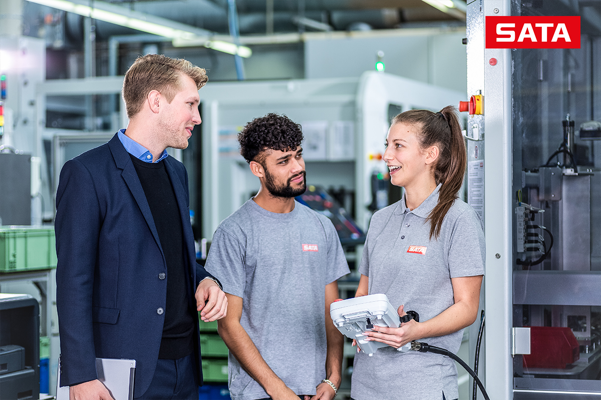 Drei Personen besprechen technische Abläufe in einer industriellen Produktionsumgebung.