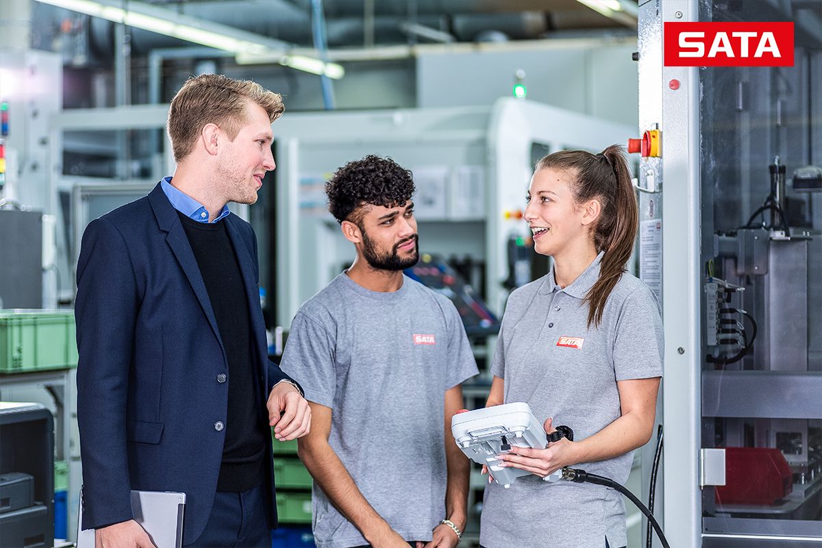 Drei Personen besprechen technische Abl&auml;ufe in einer industriellen Produktionsumgebung.