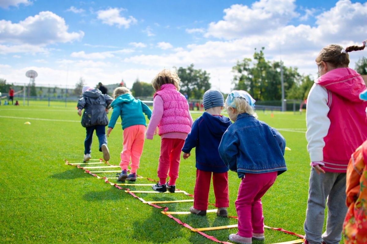 Kinder laufen über eine Koordinationsleiter auf dem Sportplatz.