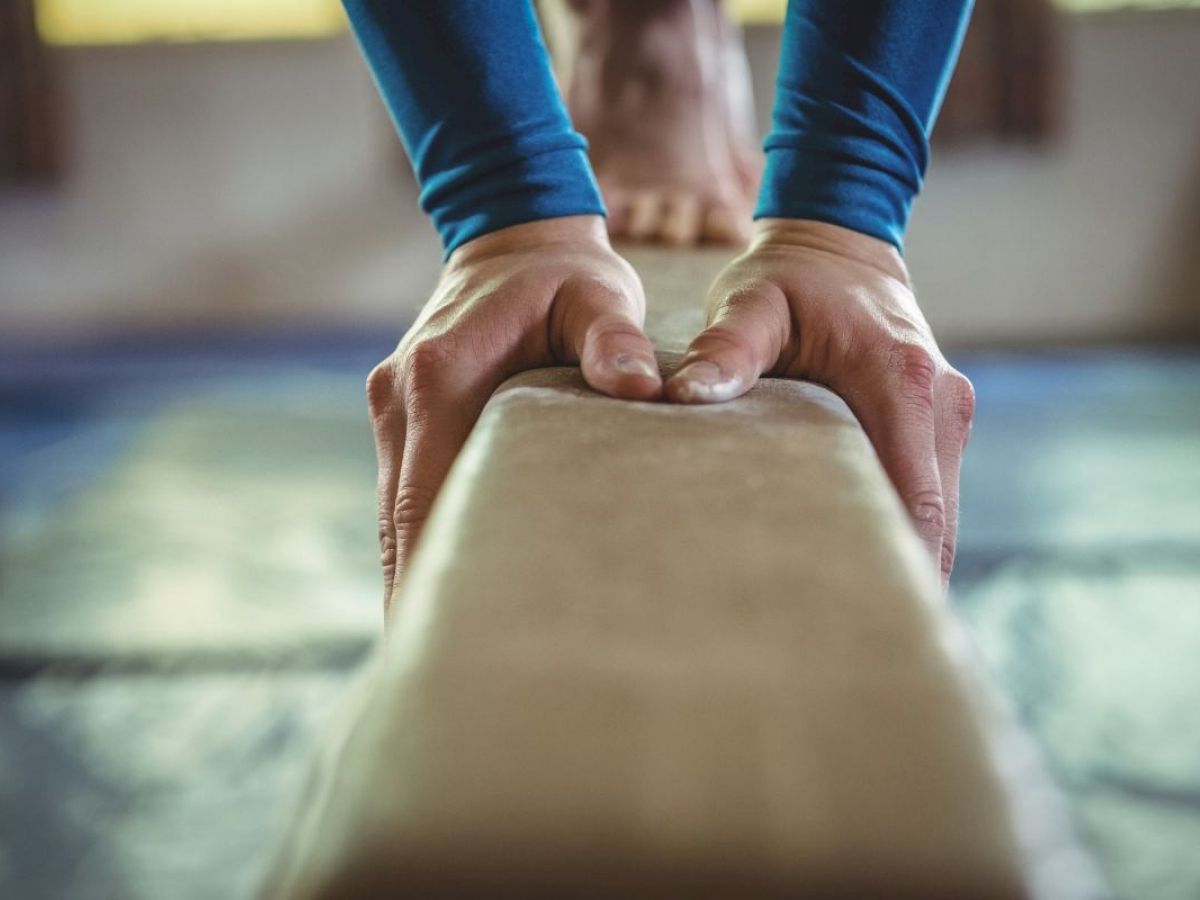 Hände einer Turnerin greifen den Schwebebalken während einer Übung.