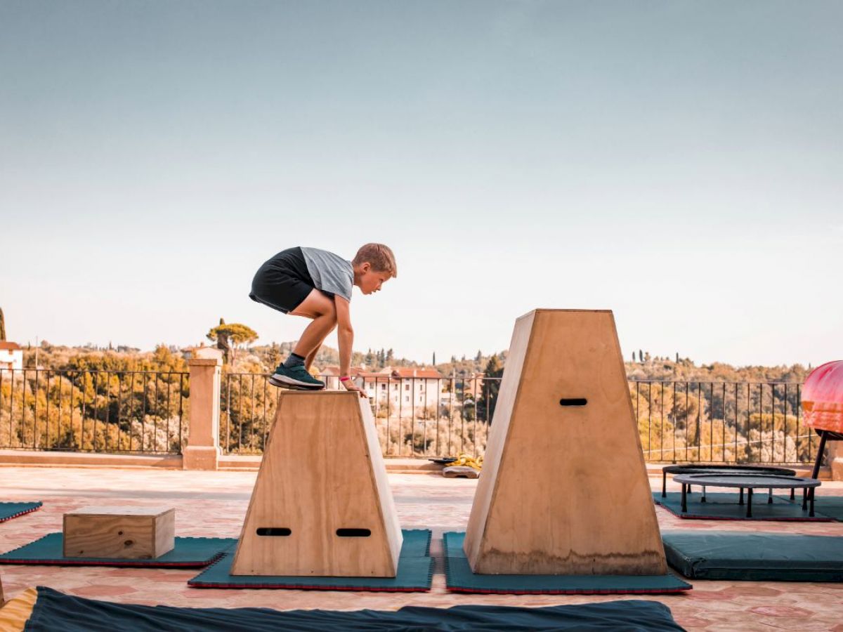 Kind bewegt sich über Parkour‑Elemente auf einer Terrasse.