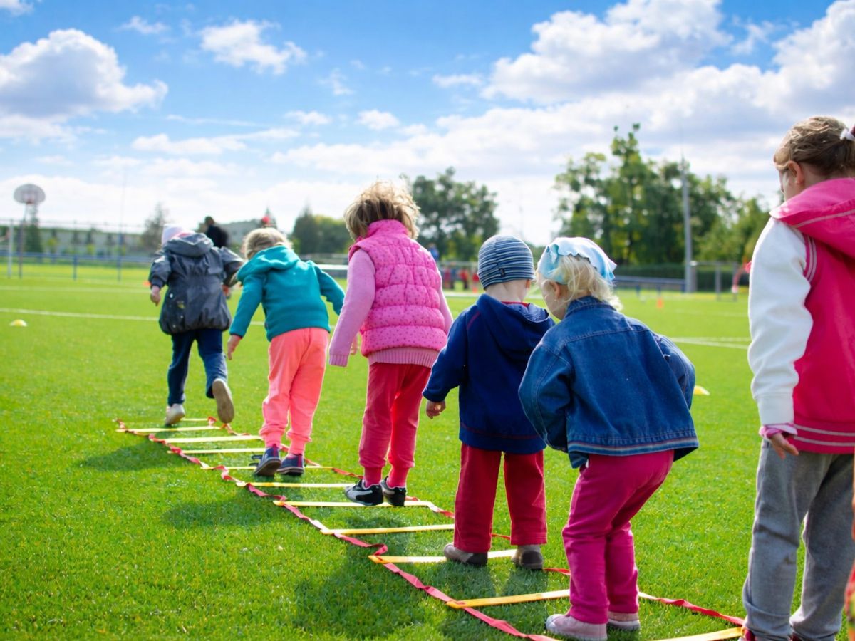 Kinder laufen über eine Koordinationsleiter auf dem Sportplatz.